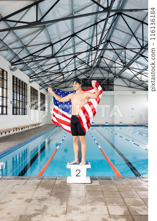 Caucasian young male swimmer holding American flag stands by the pool indoors 116136184