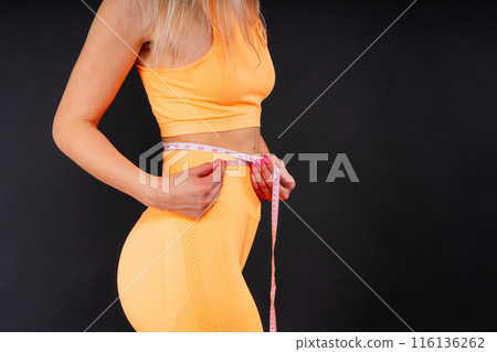 A weight loss and healthy lifestyle concept. Smiling slim woman measuring her waist with tape 116136262