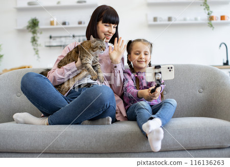 Mother and daughter taking selfie with cat on couch 116136263