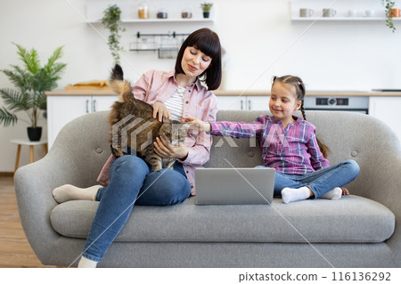 Mother and daughter bonding with cat while using laptop at home Mother and daughter bonding with cat while using laptop at home 116136292