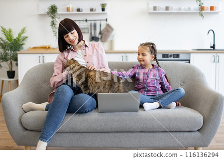 Mother and daughter with cat relaxing on sofa with laptop 116136294