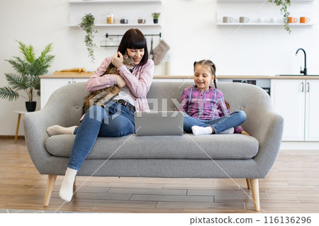 Mother and daughter using laptop on cozy living room sofa Mother and daughter using laptop on cozy living room sofa 116136296