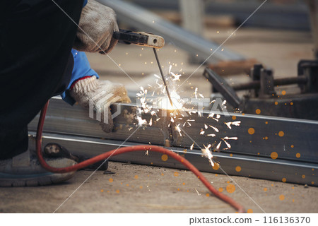 Construction Worker hands using Welding machinery iron metal sparking. Men hands wear protective glove Hot flame metal work cutting fire iron workshop. Locksmith use Welding machine cut metal process Construction Worker hands using Welding machinery iron metal sparking. Men hands wear protective glove Hot flame metal work cutting fire iron workshop. Locksmith use Welding machine cut metal process 116136370