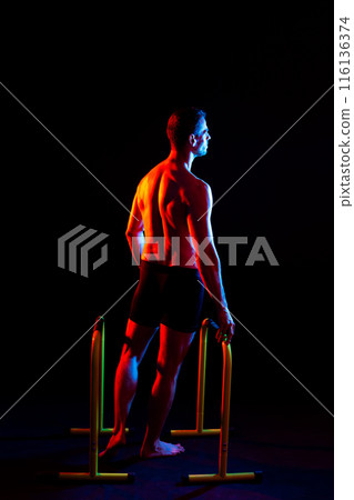 Strong male athlete shows moves on parallel bars, studio shot 116136374