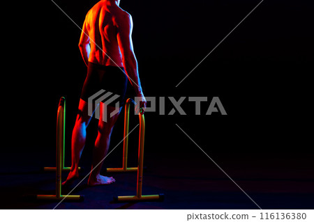 Strong male athlete shows moves on parallel bars, studio shot 116136380