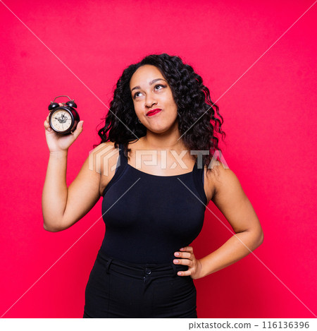 Shocked young woman holding an alarm clock, emotional african american female student late to study 116136396