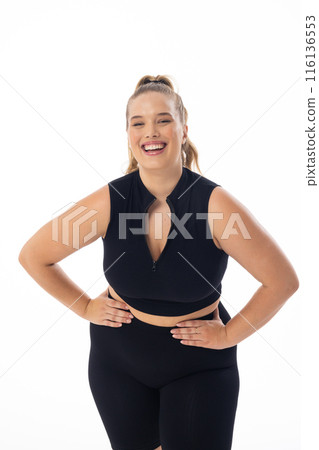 A young Caucasian plus-size model in black sportswear stands on white background, copy space A young Caucasian plus-size model in black sportswear stands on white background, copy space 116136553
