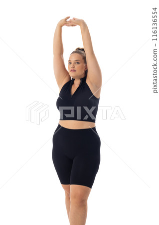 Caucasian plus-size model stretches arms up, clad in black sportswear on white background 116136554