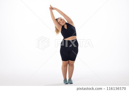 Caucasian plus-size model in sportswear stretches on a white background 116136570