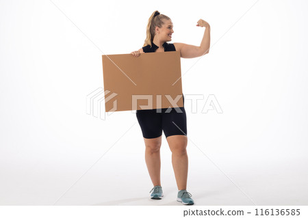 Plus size Caucasian woman shows strong arm, holds sign on white background, copy space Plus size Caucasian woman shows strong arm, holds sign on white background, copy space 116136585