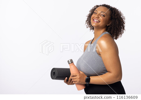 A biracial young female plus size model holds yoga mat and water bottle, copy space A biracial young female plus size model holds yoga mat and water bottle, copy space 116136609