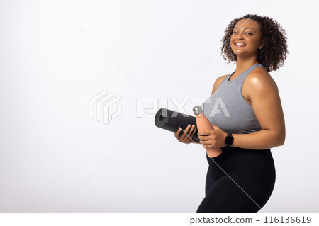 Biracial young female plus size model holds yoga mat and water bottle, copy space Biracial young female plus size model holds yoga mat and water bottle, copy space 116136619