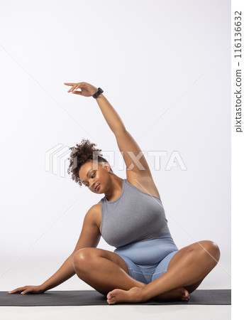 Biracial young female plus size model stretches on white background, copy space 116136632