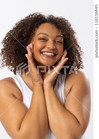 Biracial plus-size model with curly brown hair smiles, touching her face on white Biracial plus-size model with curly brown hair smiles, touching her face on white 116136645