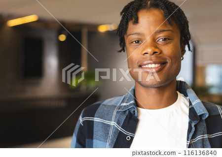 African American man standing, wearing casual clothes, smiling, in a modern business office with cop 116136840