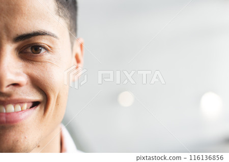 A biracial young man wearing a pink shirt, smiling at the camera in a modern business office with co 116136856