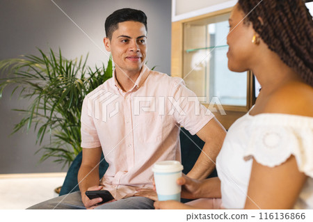 Diverse colleagues sitting, talking, holding coffee and smartphone in a modern business office Diverse colleagues sitting, talking, holding coffee and smartphone in a modern business office 116136866