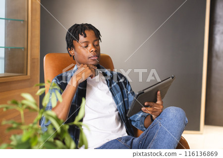 African American man holding tablet, sitting in chair, looking thoughtful in a modern business offic African American man holding tablet, sitting in chair, looking thoughtful in a modern business offic 116136869