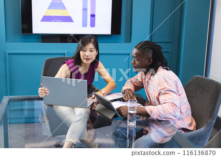 Asian woman and African American man looking at laptop screen together in a modern business office Asian woman and African American man looking at laptop screen together in a modern business office 116136870