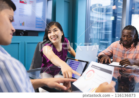 Diverse team discussing work in a modern business office, Asian woman showing tablet Diverse team discussing work in a modern business office, Asian woman showing tablet 116136873