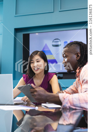 African American man and Asian woman are looking at laptop in a modern business office 116136875