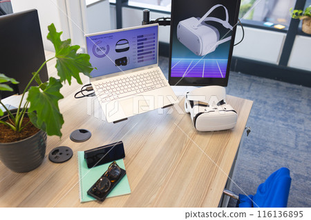 Desk with laptop displaying graphs and VR tech in contemporary business office 116136895