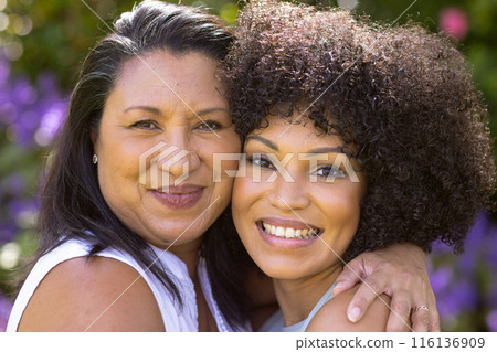 Mature biracial mother and daughter embracing, smiling in garden 116136909