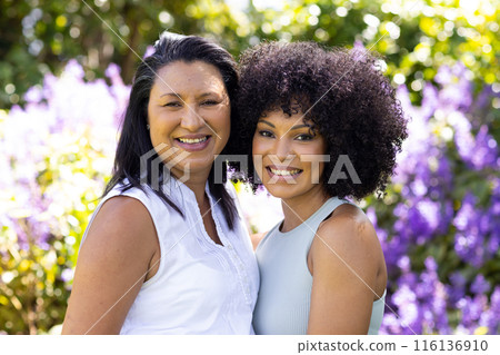 Mature biracial woman and young biracial woman stand, smiling in garden 116136910