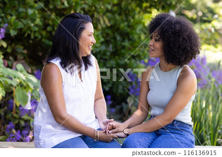 Mature and young biracial women, mother and daughter, holding hands in garden Mature and young biracial women, mother and daughter, holding hands in garden 116136915