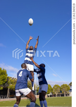 Three young African American men play rugby, one leaps for the ball Three young African American men play rugby, one leaps for the ball 116136919