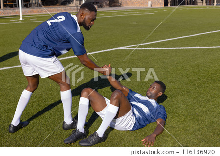 Two African American male athletes play rugby, one helping the other up Two African American male athletes play rugby, one helping the other up 116136920