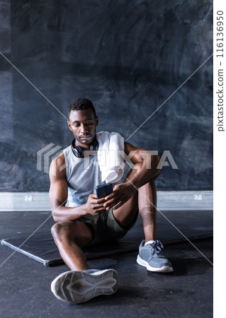 African American young male athlete sits in gym, holding a smartphone, copy space 116136950