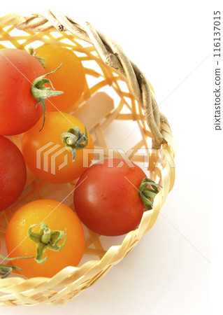 A bamboo basket full of yellow and red cherry tomatoes photographed on a white background 116137015