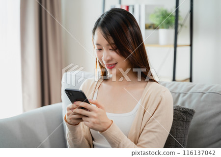 A woman is sitting on a couch and looking at her cell phone. 116137042