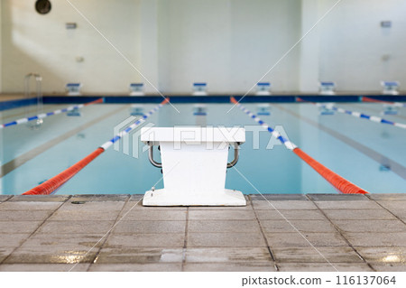 Swimmers are not visible indoors, only an empty starting block by the poolside 116137064