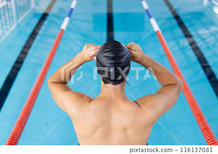 Caucasian young male swimmer adjusting swim cap at pool indoors 116137081