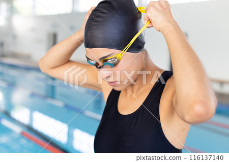 Biracial young female swimmer adjusting goggles indoors, preparing to swim 116137140