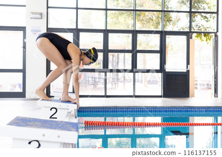 Young biracial female swimmer preparing to dive into an indoor pool, copy space 116137155