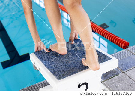 A biracial young female swimmer is preparing to dive into an indoor pool 116137169