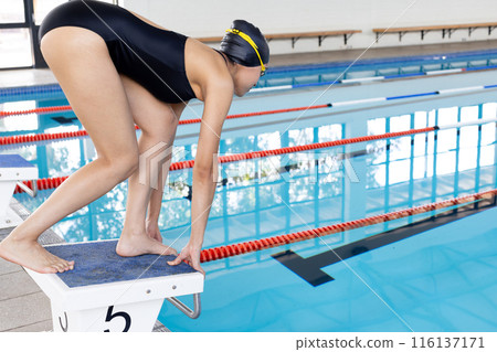 Biracial young female swimmer preparing to dive into an indoor pool, copy space Biracial young female swimmer preparing to dive into an indoor pool, copy space 116137171
