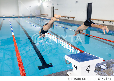 Diverse young swimmer competitors, friends diving into an indoor pool, training together 116137174
