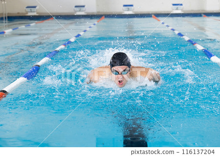 Caucasian young male swimmer training indoors in swimming pool, wearing goggles 116137204