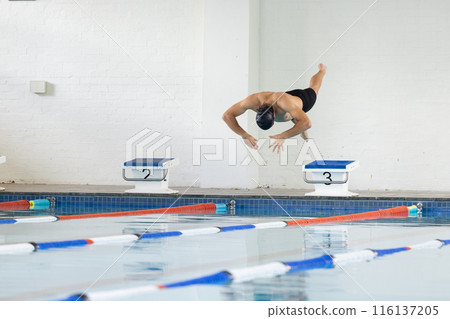 Caucasian young male swimmer diving into indoor swimming pool, wearing black cap, copy space 116137205