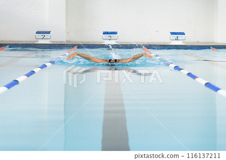 Biracial young female swimmer wearing goggles reaching end of the swimming pool lane, copy space 116137211
