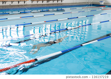 Biracial girl in swimsuit and cap trains in indoor pool, copy space 116137219