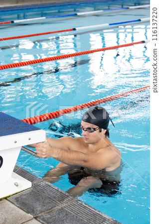Caucasian boy with dark hair in goggles prepares for an indoor swim, copy space 116137220