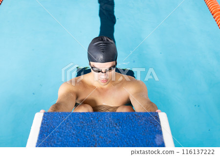 Caucasian young male swimmer preparing to dive into indoor swimming pool 116137222
