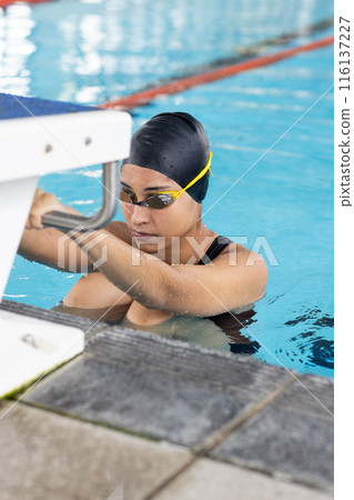 Young biracial female swimmer, grasping pool edge, ready to train 116137227