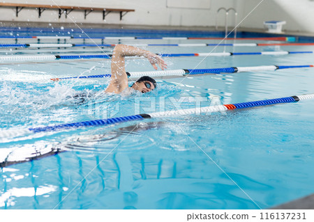 Caucasian young male swimmer wearing goggles, training indoors in swimming pool, copy space 116137231