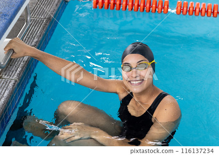 Biracial girl in goggles grips indoor pool edge Biracial girl in goggles grips indoor pool edge 116137234